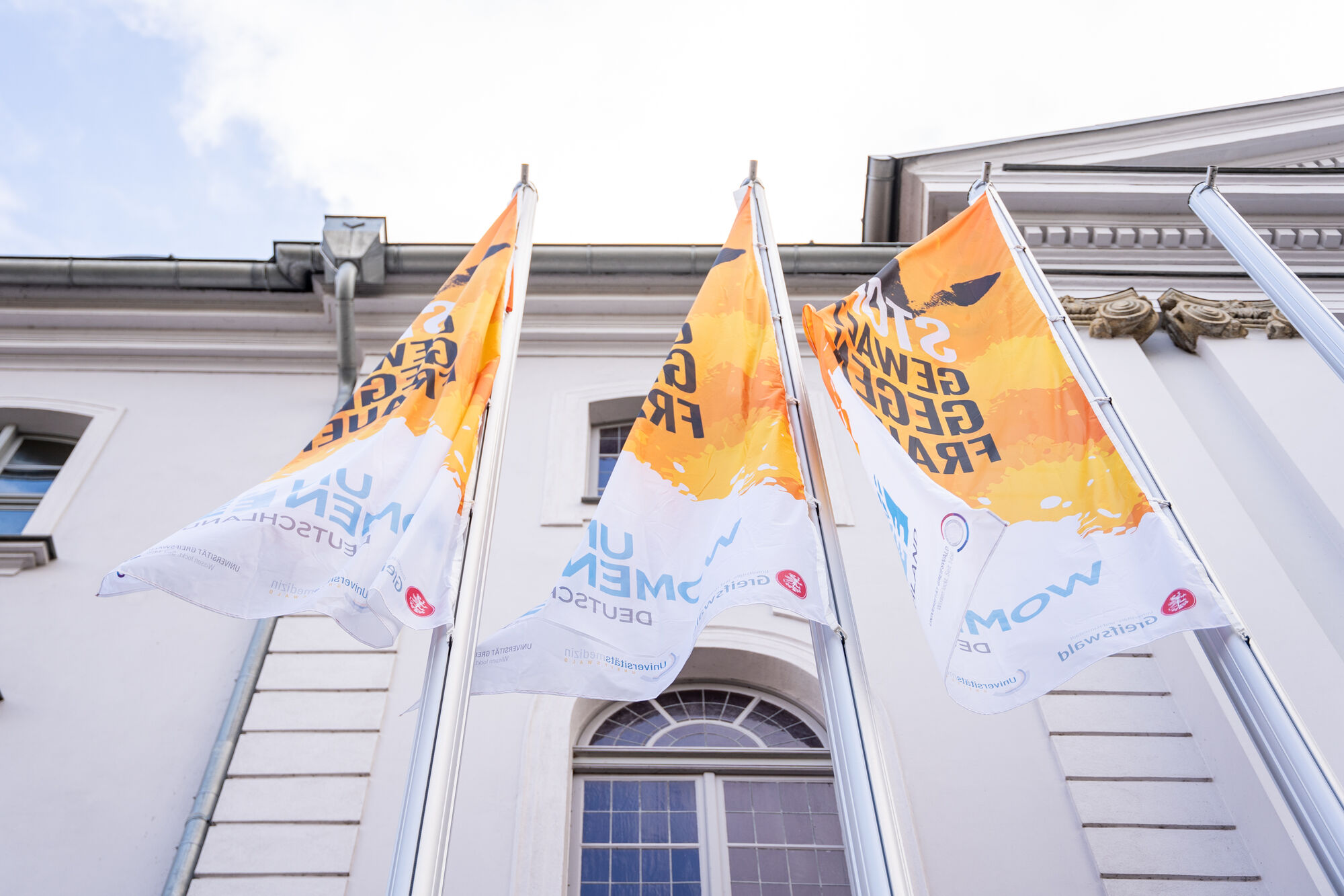 Zu sehen sind die orangen Fahnen vor dem Uni-Hauptgebäude Greifswald anlässlich des Internationalen Tages gegen Gewalt an Frauen und Mädchen.